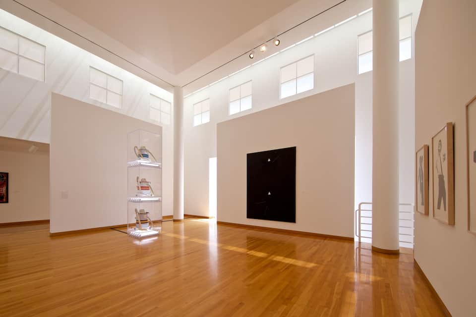 An art gallery with wooden floors, white walls, and natural light from windows.