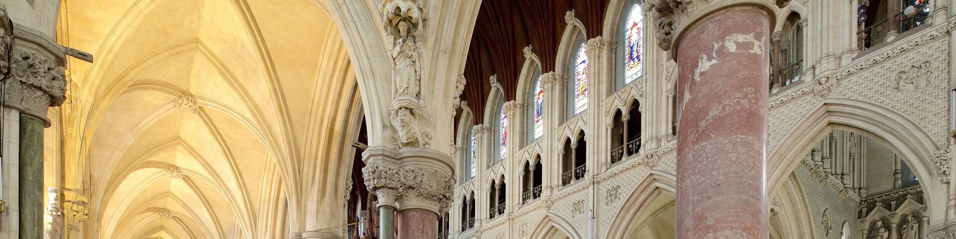 Interior de una catedral con techos abovedados altos, columnas ornamentadas y vidrieras.