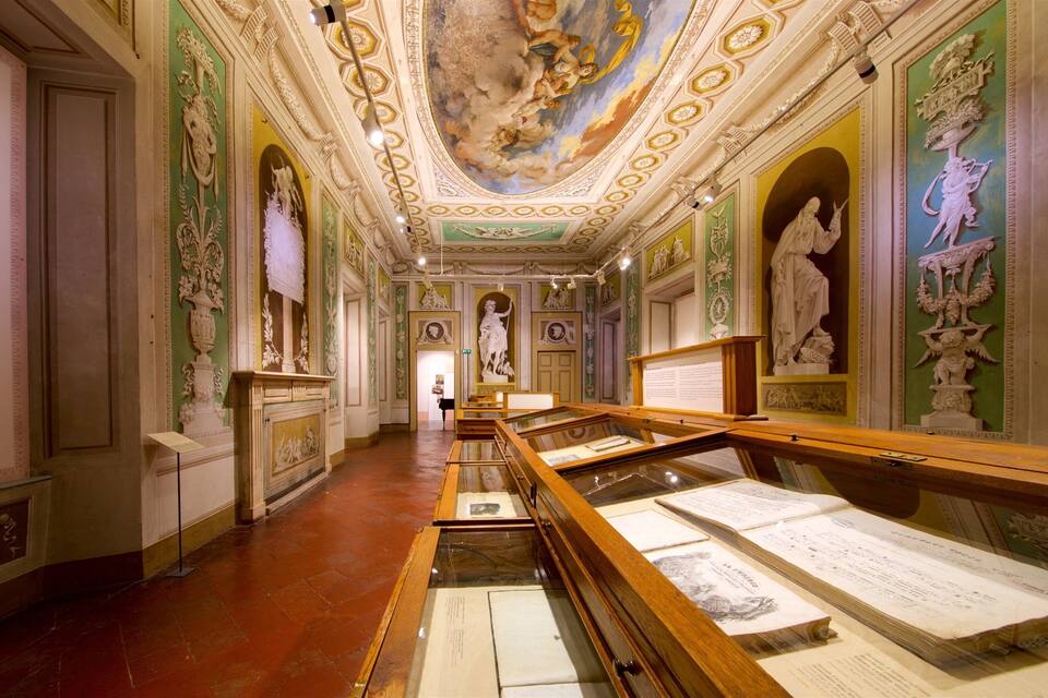 Un pasillo de museo con frescos ornamentales en el techo, estatuas clásicas y paneles informativos.