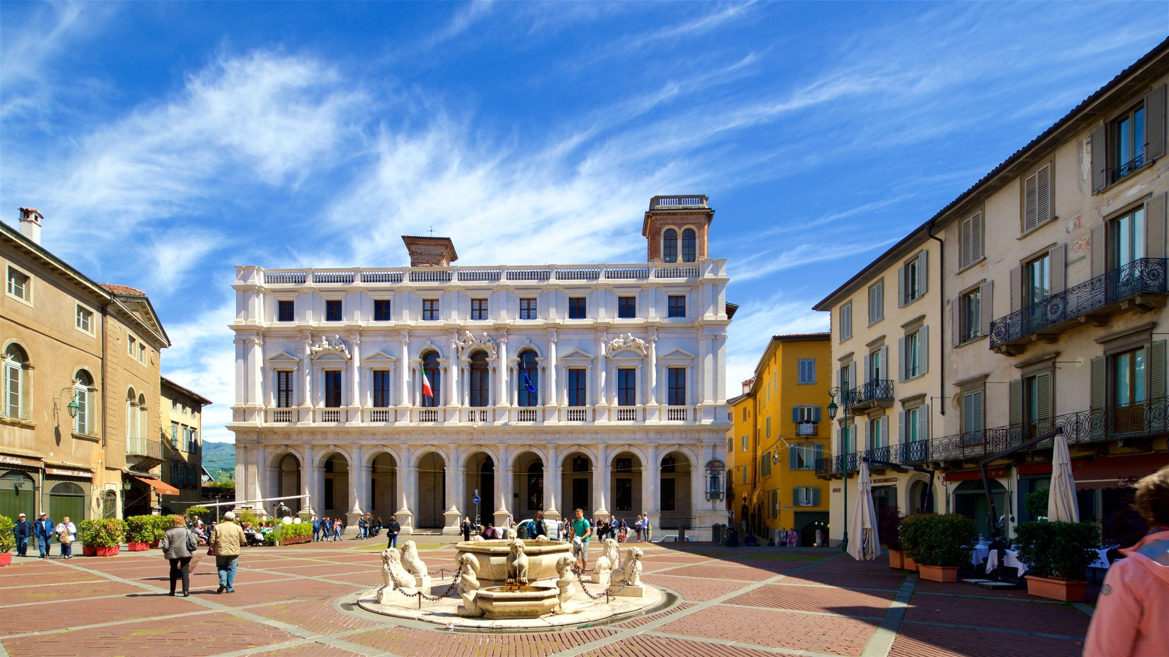 A historic building with classical architecture, a central fountain, and a bustling square with pedestrians.
