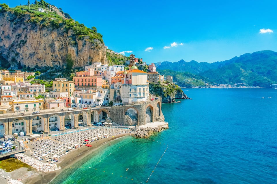 Uma vila costeira com edifícios coloridos, uma praia e um penhasco com vista para o mar.