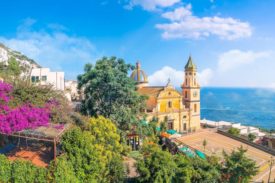 Uma vila costeira com uma igreja imponente, vegetação exuberante e vista clara para o mar.