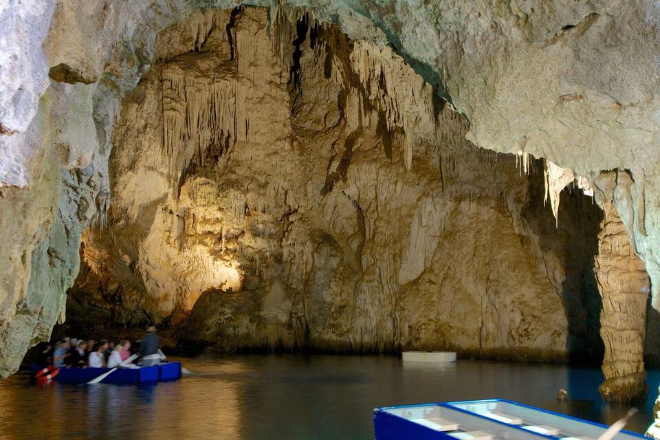 A cave with stalactites and stalagmites, a boat with people, and a water body.