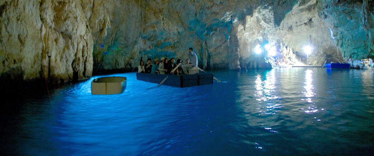 A cave with stalactites and stalagmites, a boat with people, and a boat with a blue container.