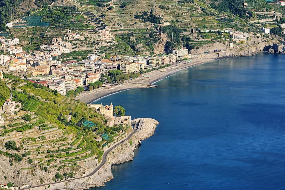 A coastal town with terraced vineyards, a castle, and a beach.