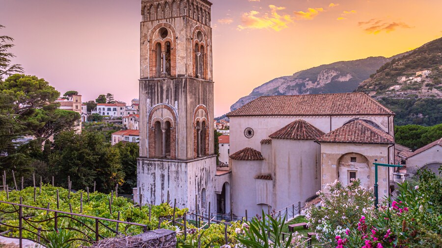 Ravello, Italy. August 9th, 2020. Breathtaking sunset over the Ravello Cathedral and its bell tower framed between plants and colorful oleander flowers.