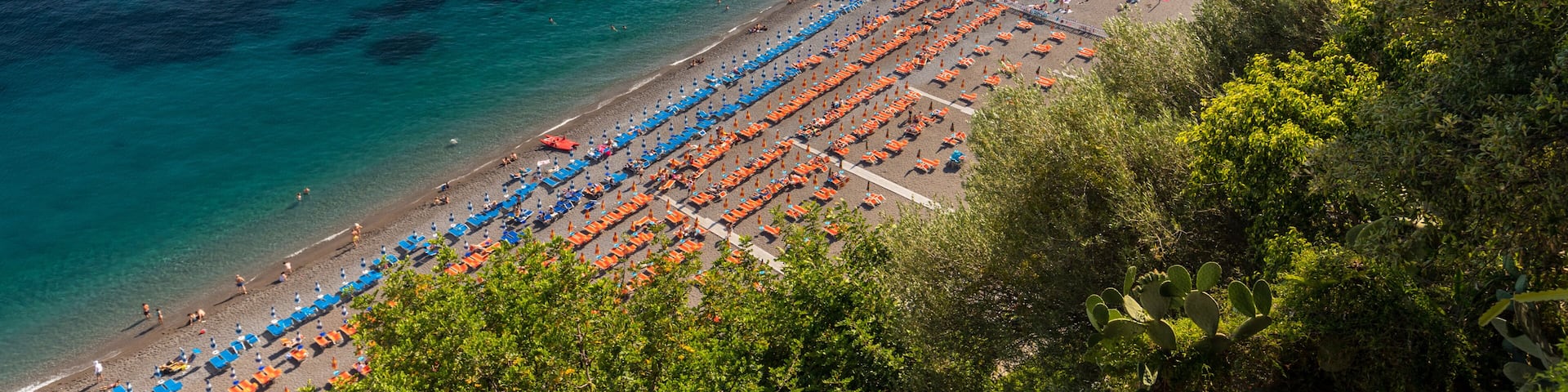 The main beach in Positano, Spiaggia Grande, with its bright orange and blue beach umbrellas and the sparkling blue sea of the Amalfi Coast.