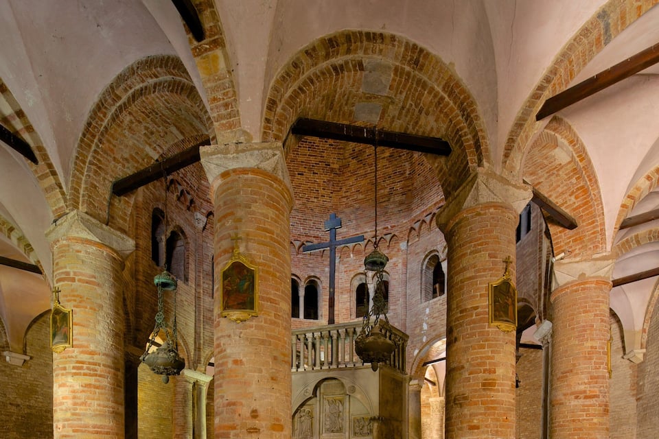 An interior with arched brick ceilings, columns, and a central cross.