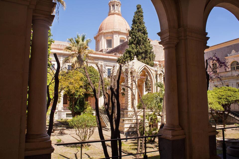 A historic building with a dome and arches, surrounded by trees and a clear sky.