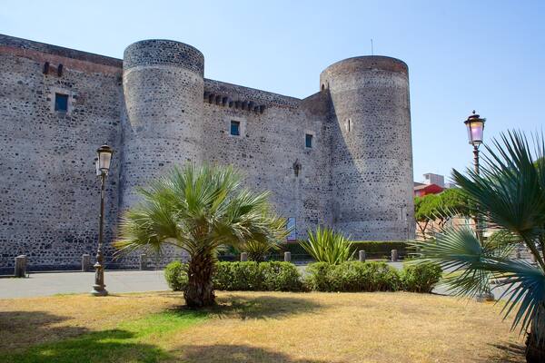 Un château historique en pierre, doté de deux tours rondes et d’un jardin bien entretenu où l’on peut admirer des palmiers.