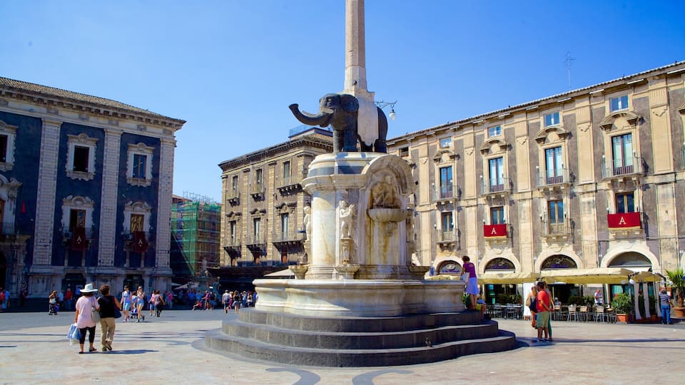 A public square with a central monument featuring an elephant statue, surrounded by historic buildings with balconies and signage.