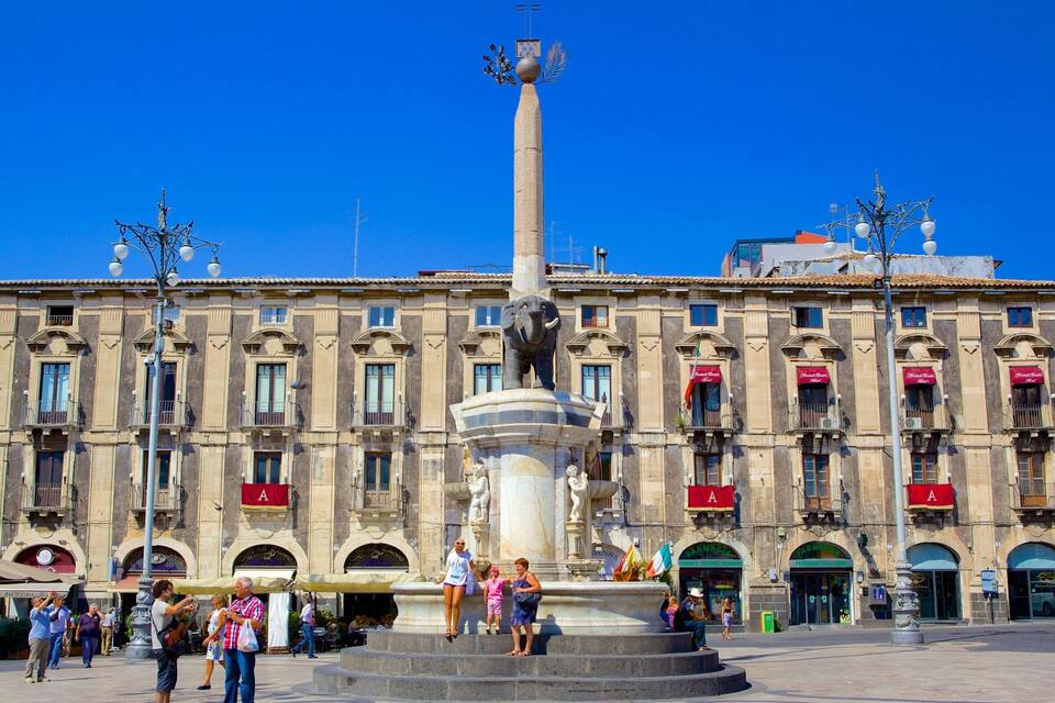 A historic building with a central monument, people around, and shops with red awnings.