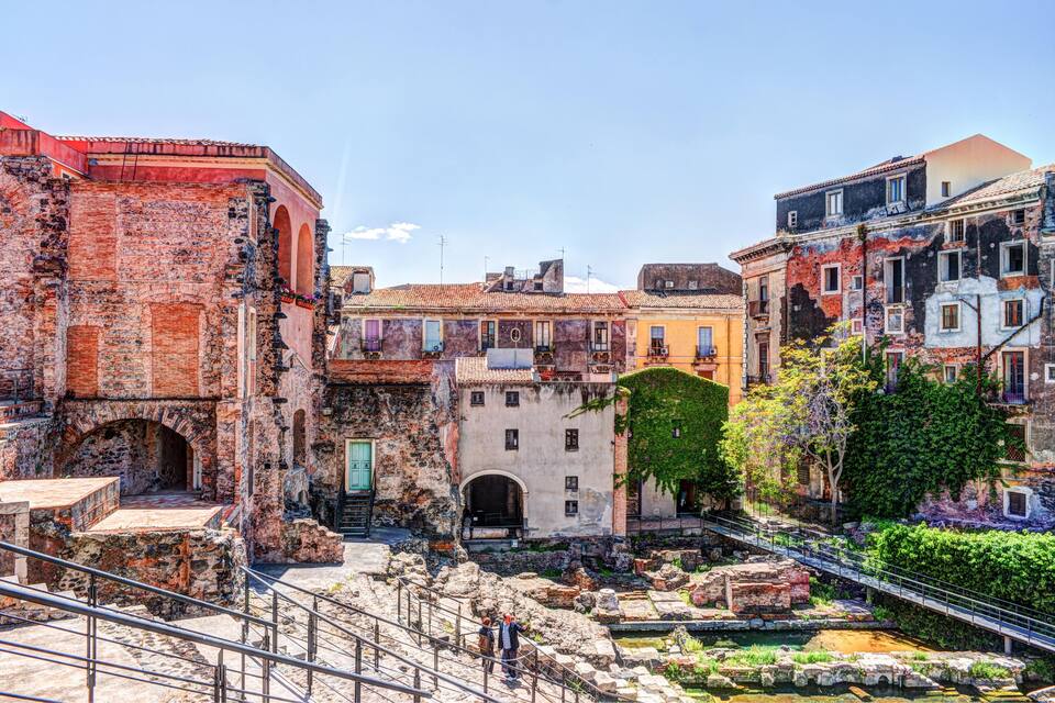 Una plaça històrica amb ruïnes antigues, un petit pont i edificis de colors.