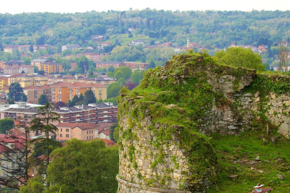 Mur de pedra històric amb vegetació, un poble amb edificis de colors i un turó forestal al fons.