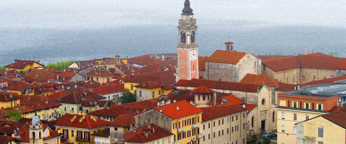 A coastal town with red-roofed buildings, a prominent clock tower, and a view of the sea.