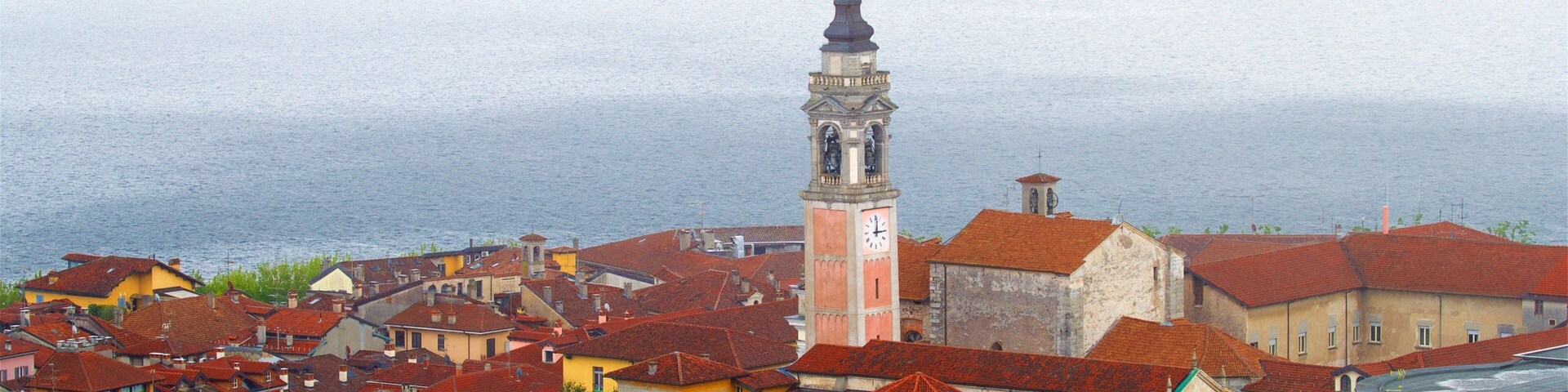 A coastal town with red-roofed buildings, a prominent clock tower, and a view of the sea.
