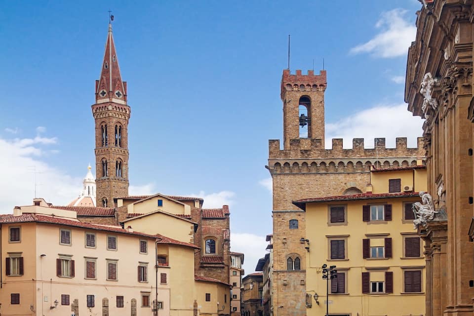 A narrow street flanked by historic buildings with a prominent tower and a smaller turreted structure.