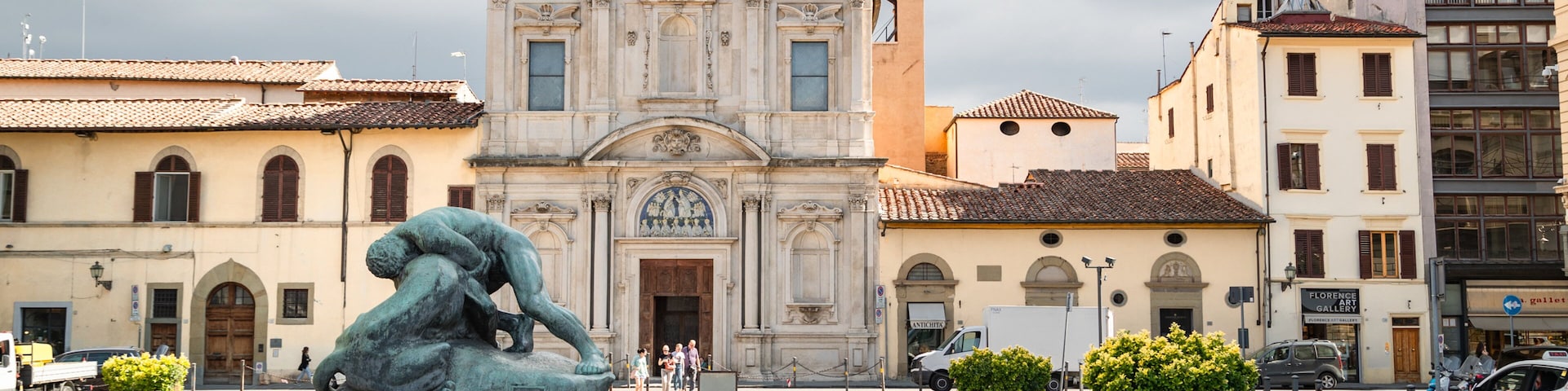 Uma praça com uma estátua, uma igreja e edifícios ao redor.