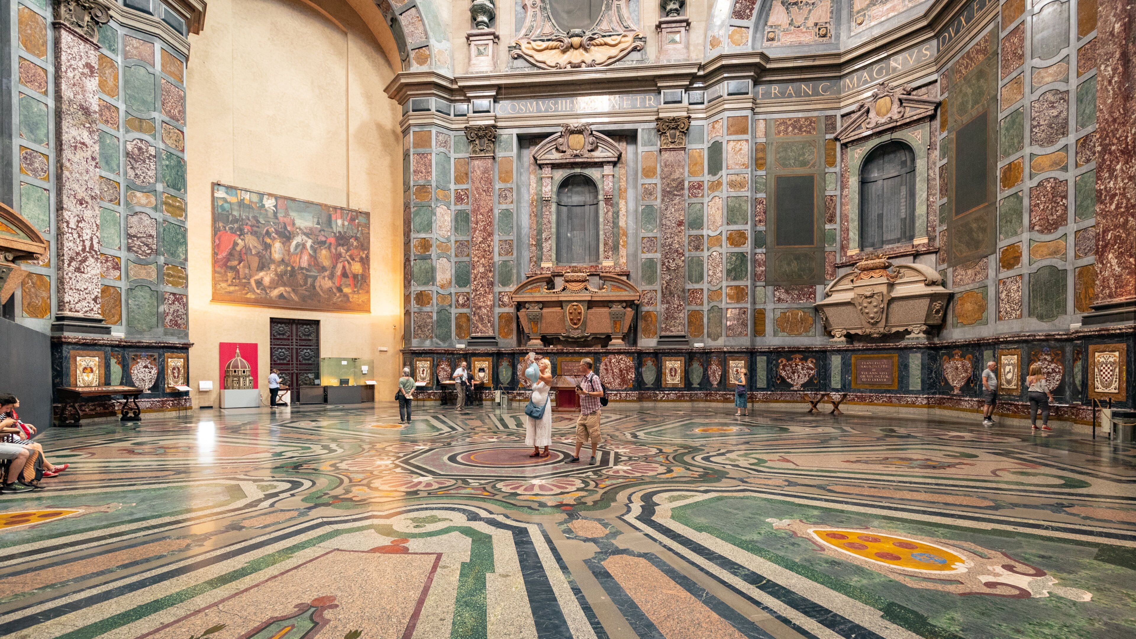 A grand hall with ornate marble floors, a large fresco on the wall, and intricate architectural details.