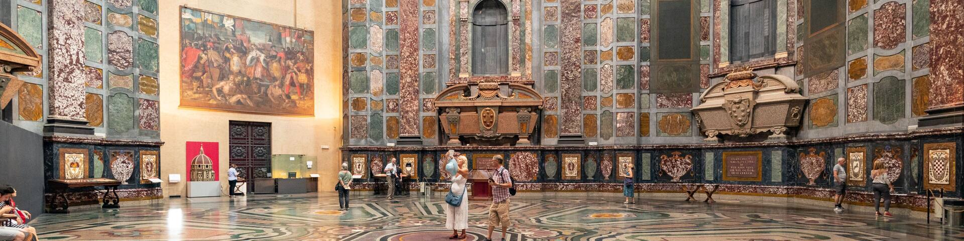 A grand hall with ornate marble floors, a large fresco on the wall, and intricate architectural details.