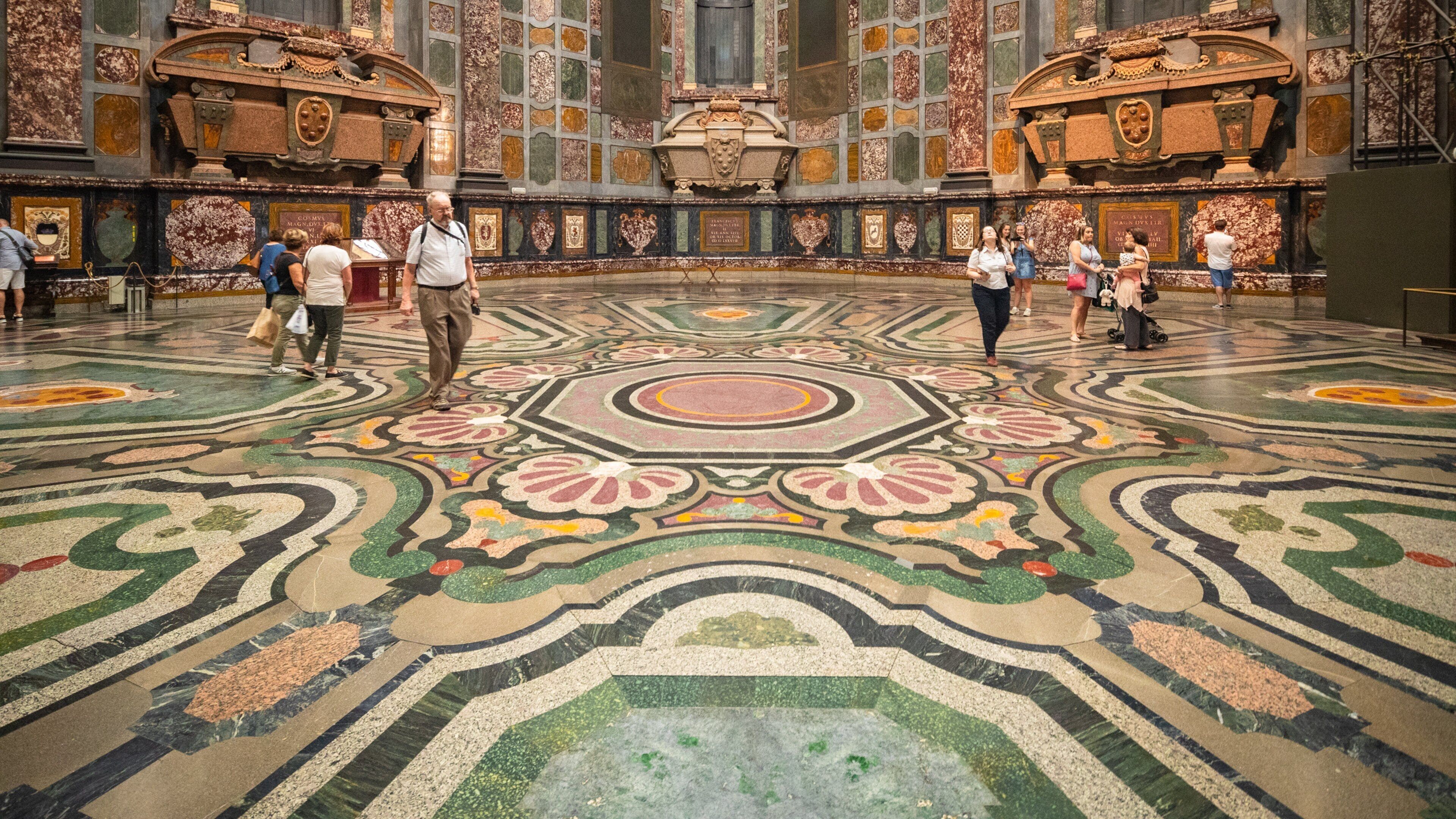 A grand hall with a detailed mosaic floor and ornate decorations.