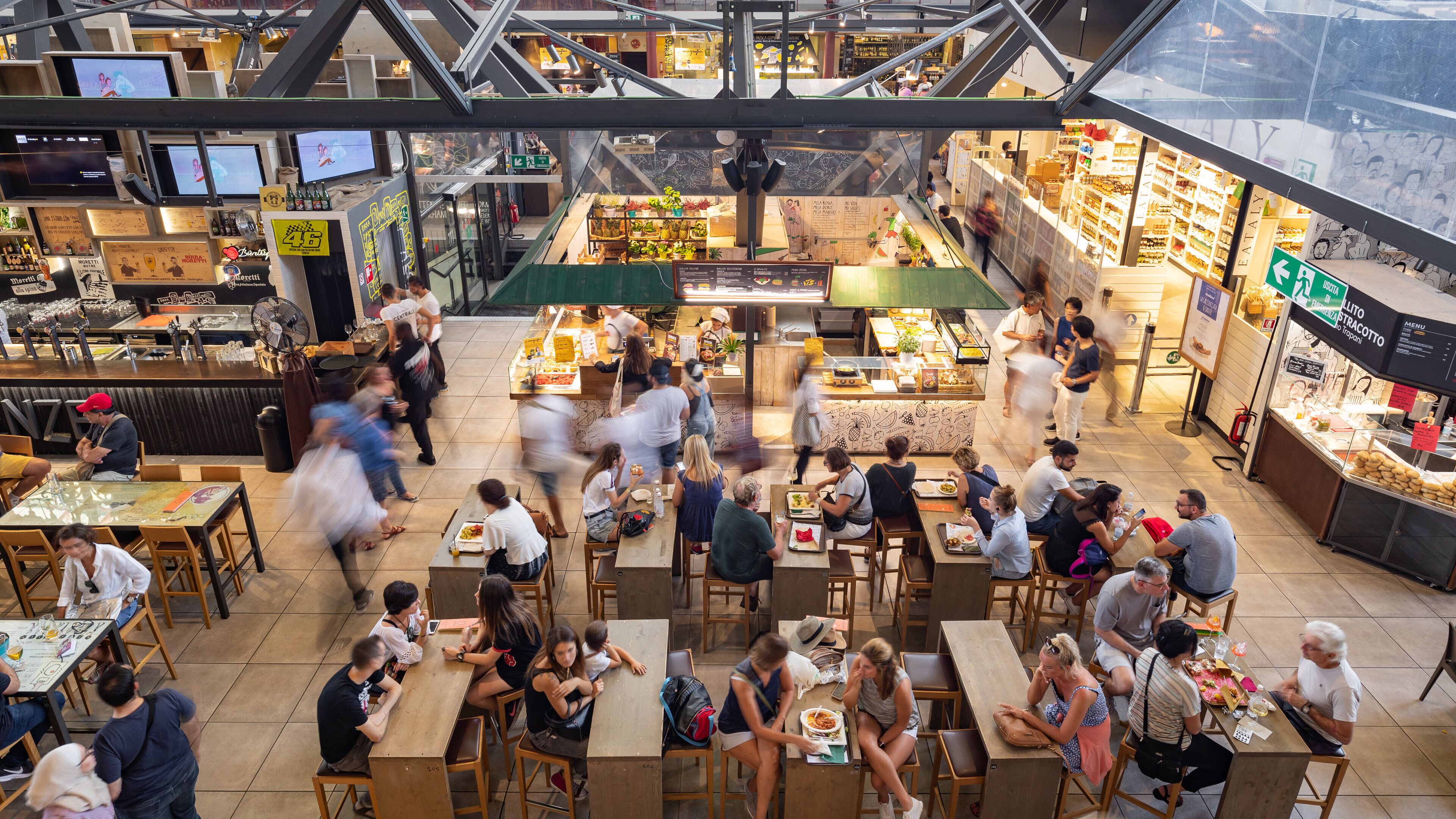 A bustling indoor market with various stalls and tables where people are dining and shopping.