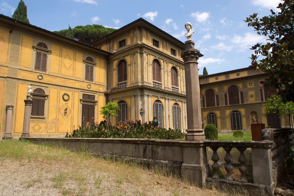 A historic building with classical architecture, a statue, and a well-maintained garden.