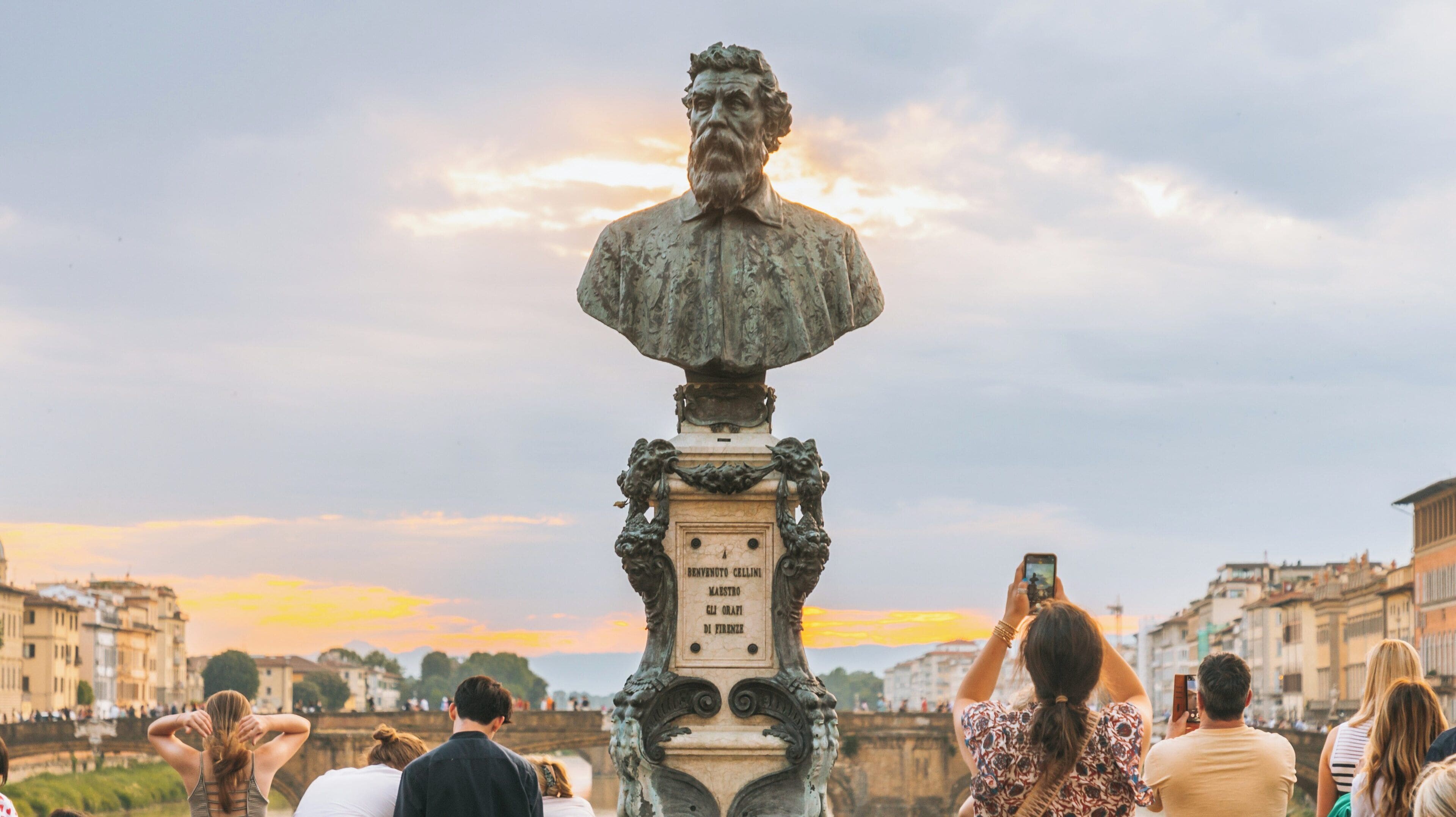 Visitors admire the statue of a notable figure at Ponte Vecchio as the sun sets over Florence in the Oltrarno district of Tuscany, Italy