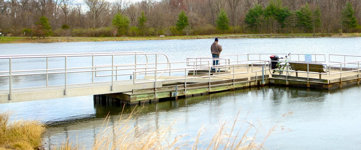 A wooden pier extending over a calm lake with a person fishing.