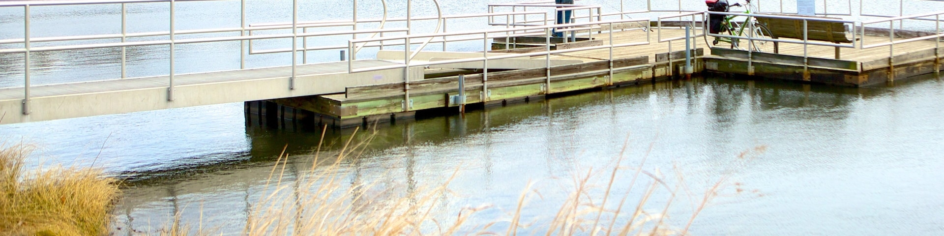 A wooden pier extending over a calm lake with a person fishing.