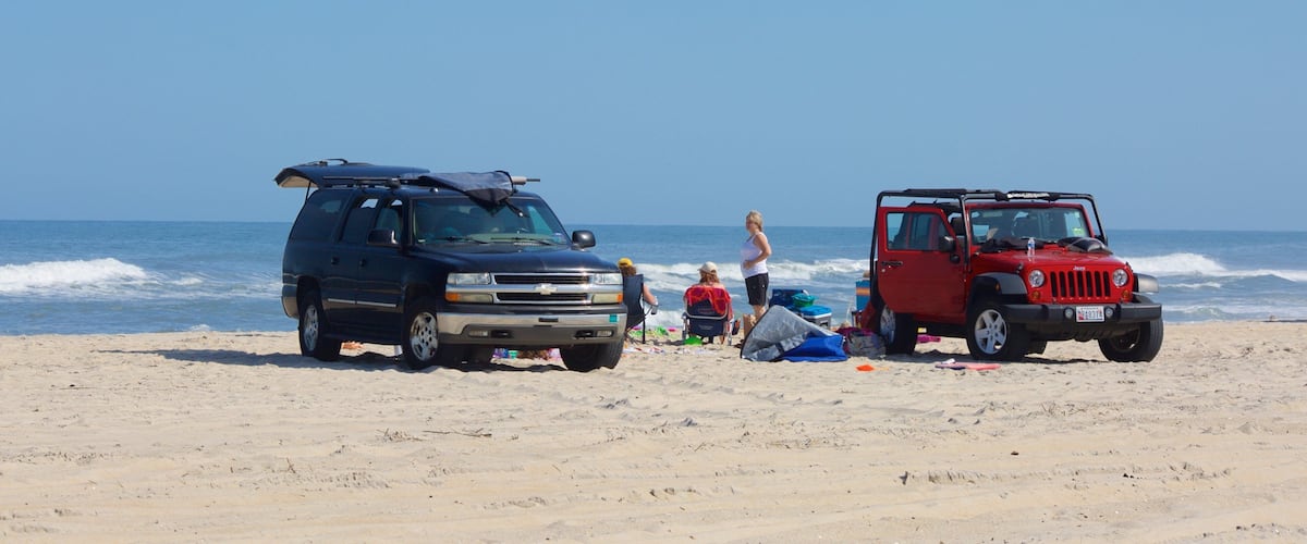 Two vehicles parked on a sandy beach with the ocean in the background.