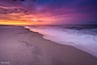 Uma praia ao pôr do sol com um céu colorido.