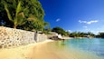 A beach with clear turquoise water, a stone wall, and lush greenery.