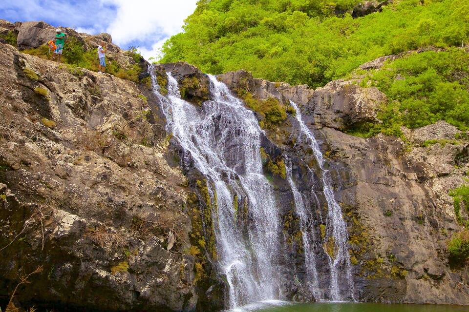 A multi-tiered waterfall cascading down a rocky cliff surrounded by lush greenery.