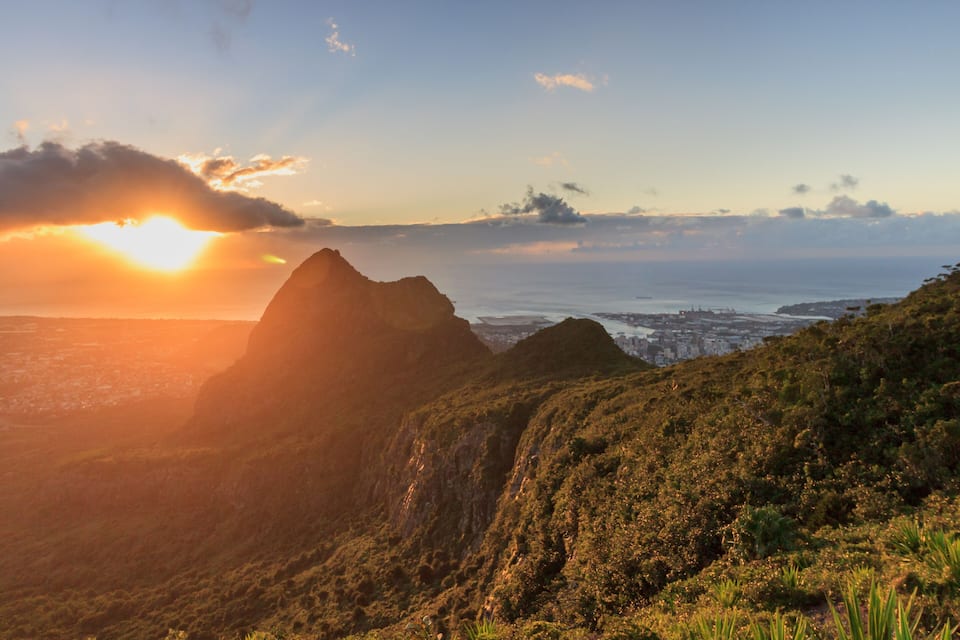 A mountainous landscape with a city in the distance and a sunset.