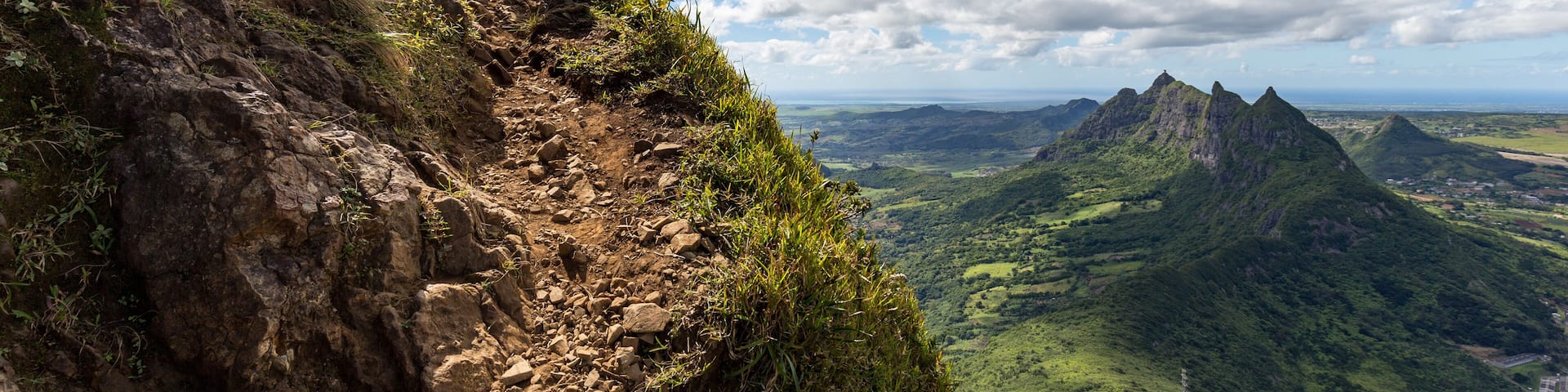 Two persons climbing up the trail to the peak of the mountain Le Pouce on the island of Mauritius with a view over Pieter Both.