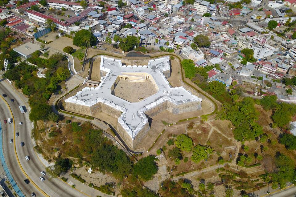 Vista aérea de uma fortaleza histórica cercada por uma área urbana densa com edifícios modernos.