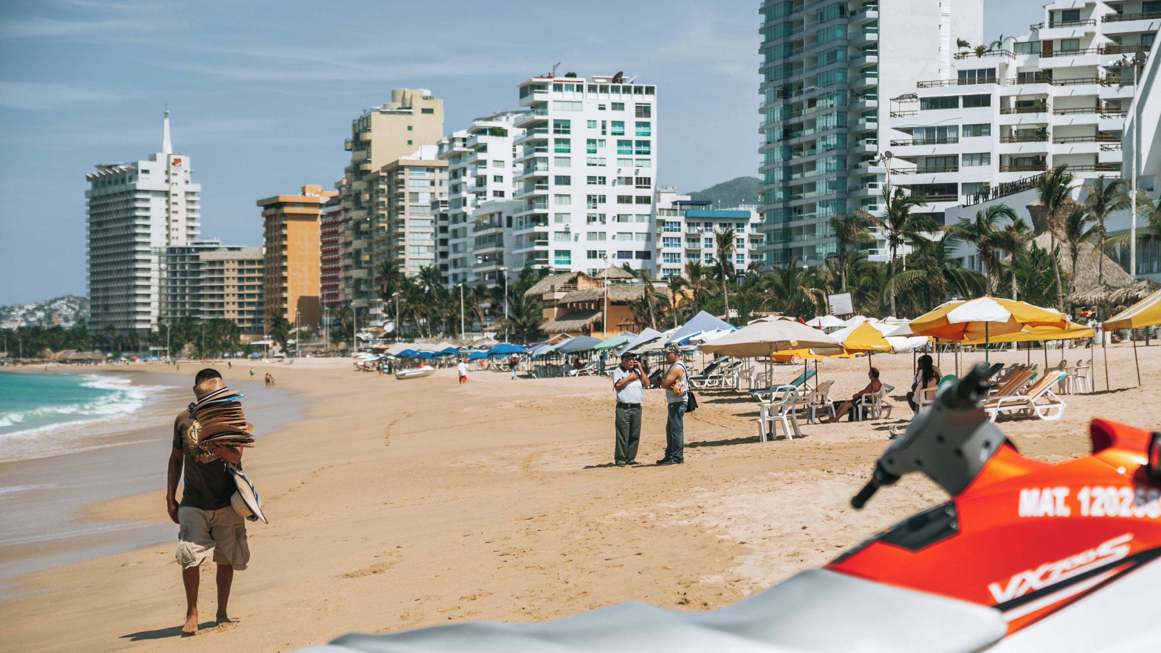 Beautiful day at Condesa Beach in Acapulco where visitors relax under umbrellas and locals offer crafts and amenities