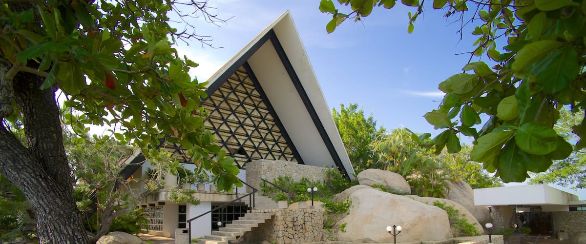 Un edificio moderno con fachada geométrica, rodeado de rocas grandes y exuberante vegetación.