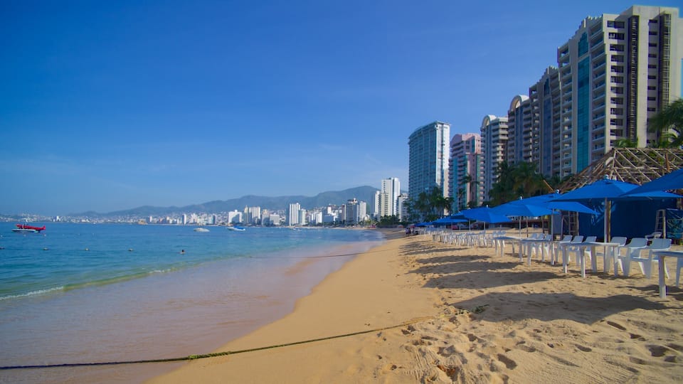 A beach with a clear blue sky, sandy shore, and tall buildings in the background.