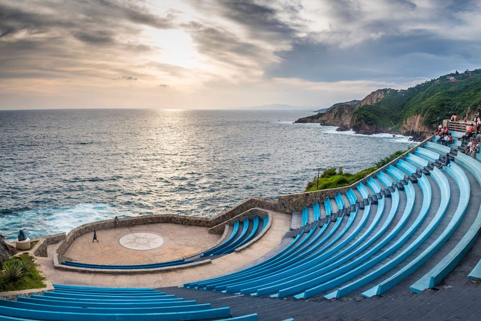 Ein Amphitheater am Meer mit blauen Stufen und einer runden Bühne, mit Blick auf den Ozean.