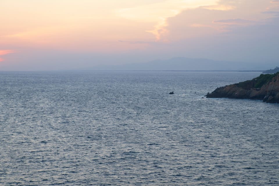 Um pôr do sol sobre um mar calmo com uma costa rochosa.