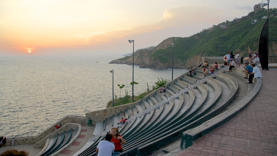 Um anfiteatro à beira-mar com pessoas sentadas nos degraus ao pôr do sol.