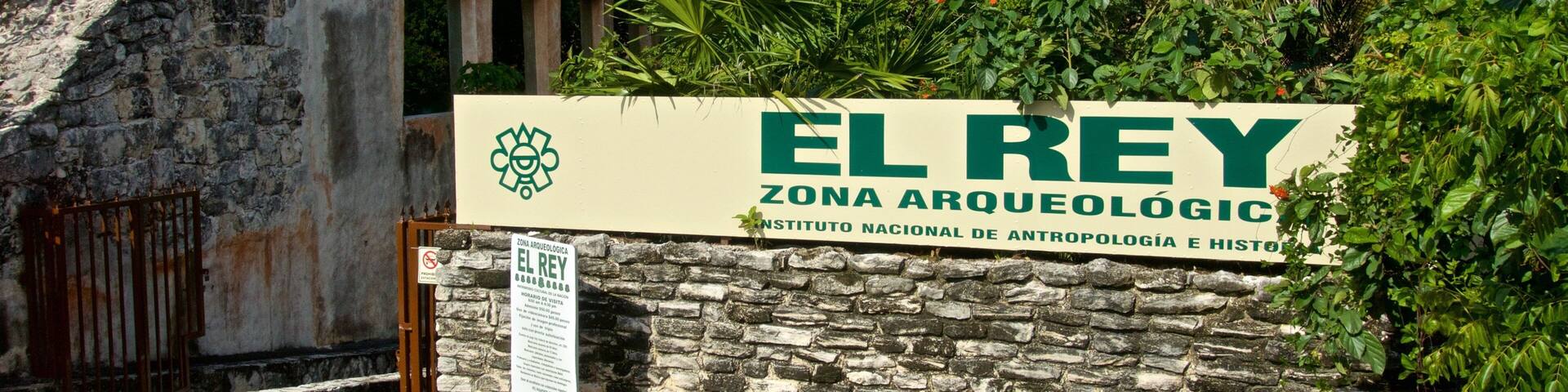 A stone wall with a sign for 'El Rey Archaeological Zone' and a logo for the National Institute of Anthropology and History.