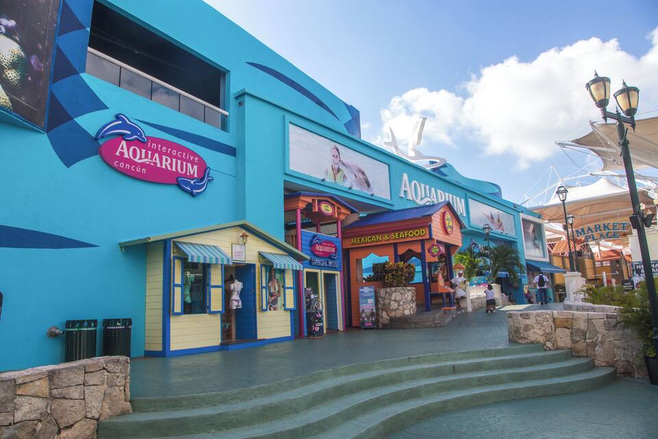 The exterior of the Interactive Aquarium Cancun, featuring a blue facade, a Mexican & Seafood restaurant, and a Market Place.