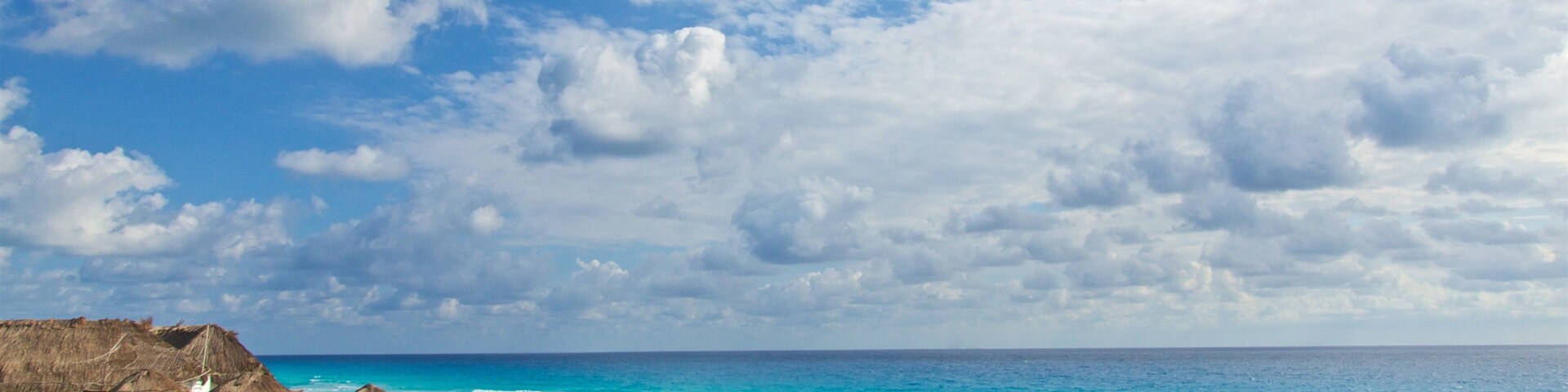 Una playa con sombrillas de paja, aguas turquesas cristalinas y un cielo parcialmente nublado.