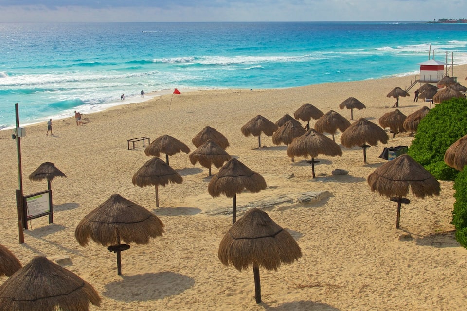 Uma praia com guarda-sóis de palha e uma torre de salva-vidas.