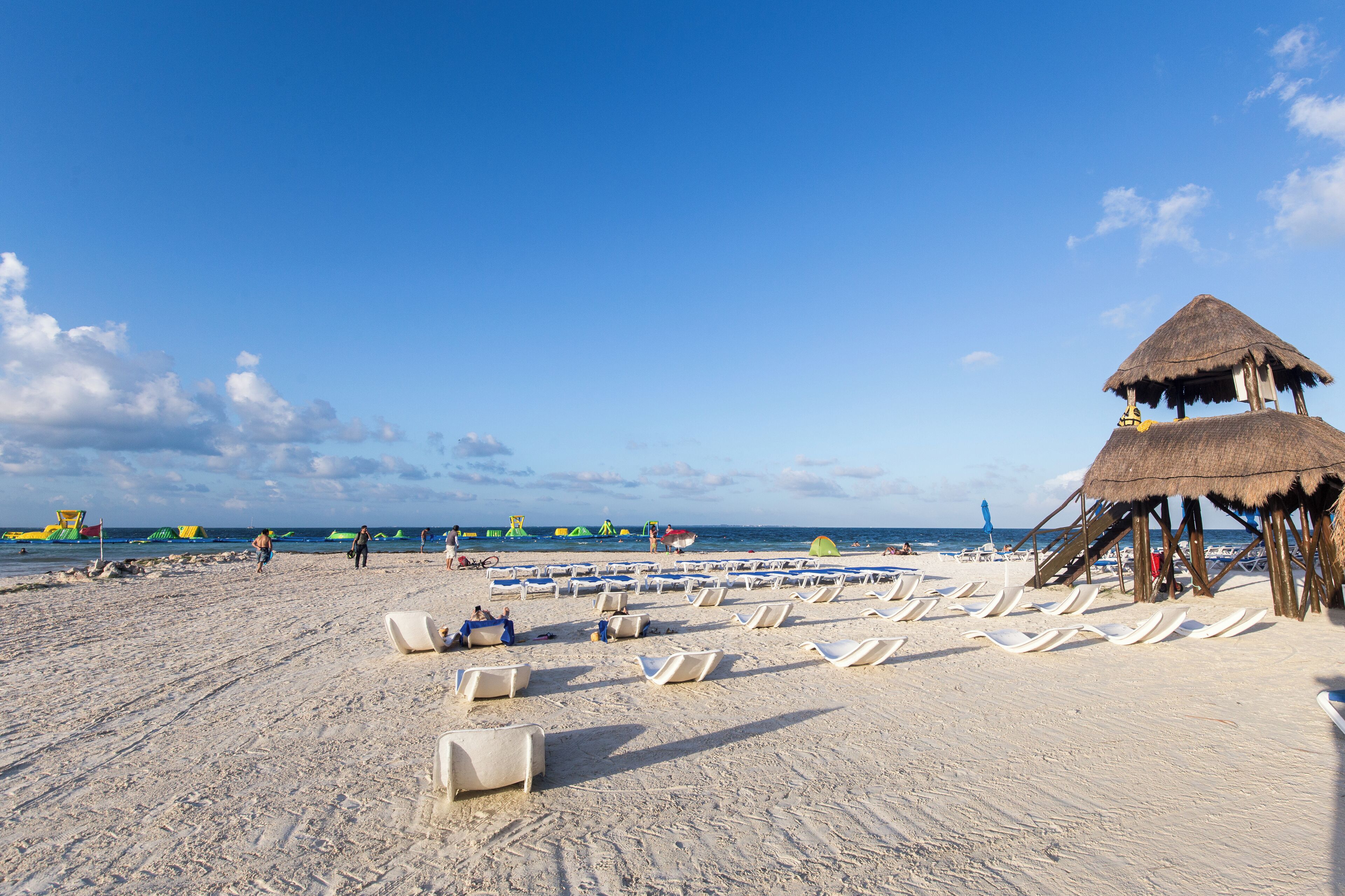 A beach with rows of sun loungers and a thatched-roof structure.