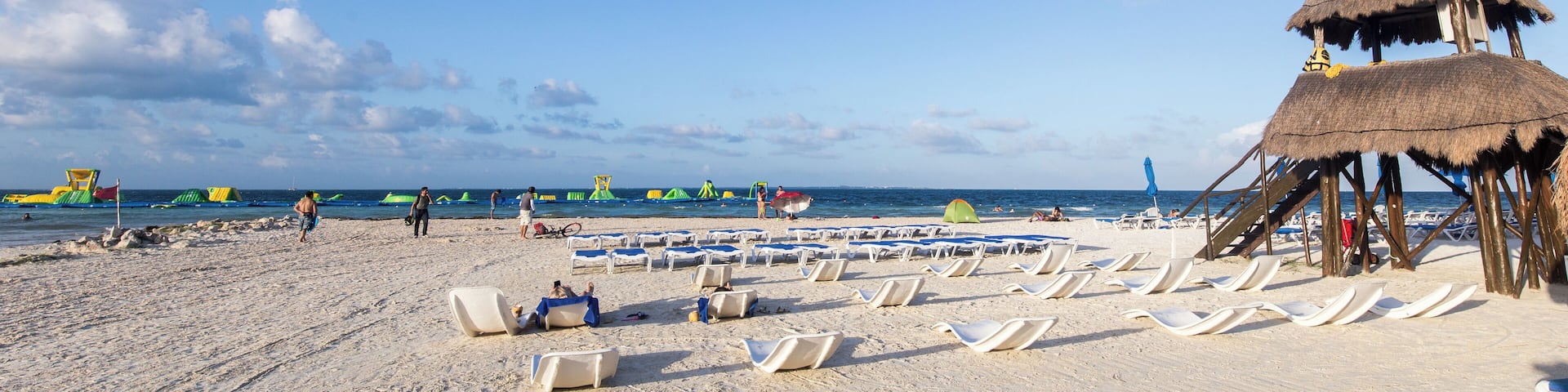Una playa con filas de tumbonas y una estructura de techo de paja.