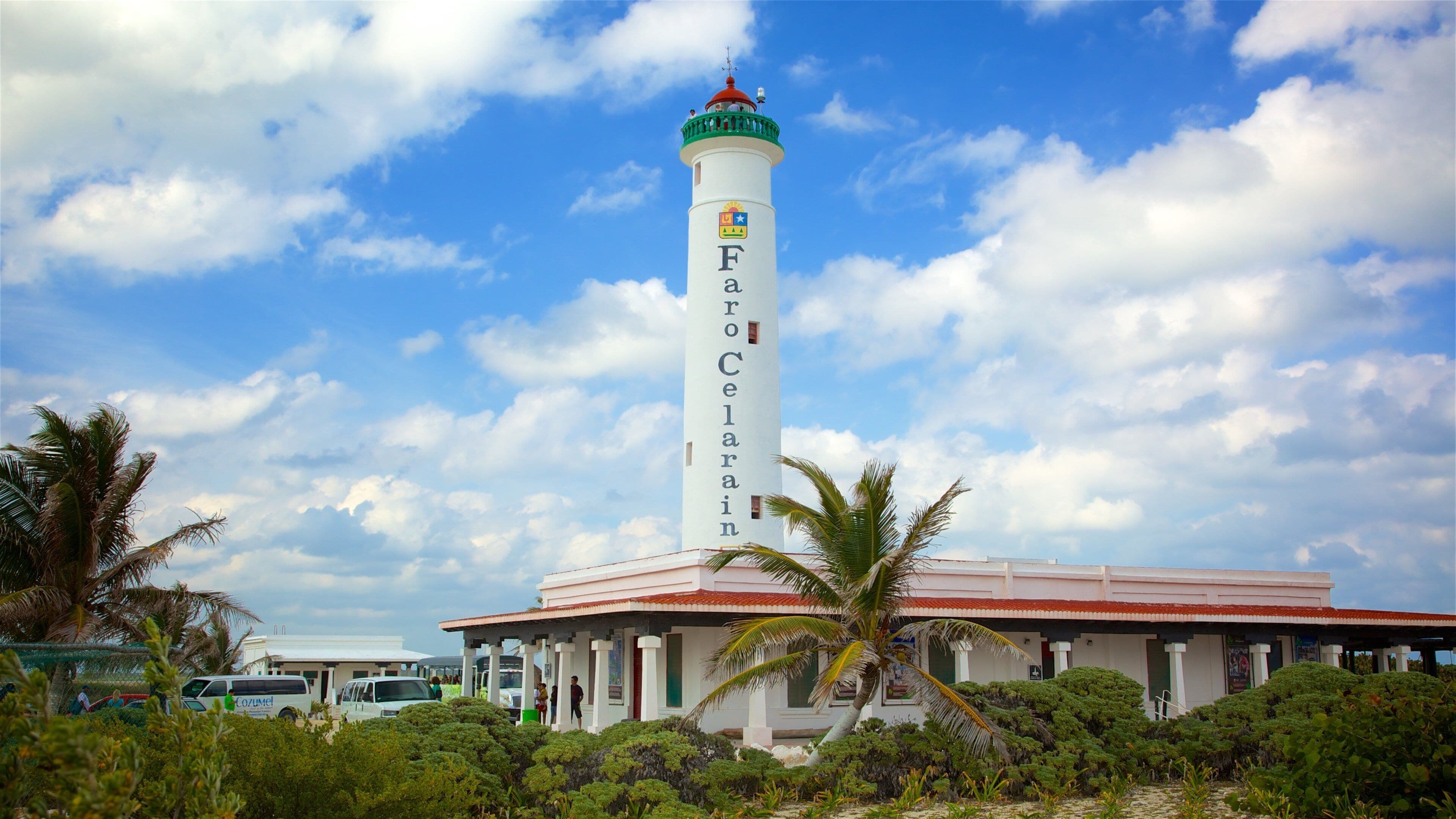 A lighthouse named Farro Celenar with a red roof and white walls, surrounded by lush greenery and palm trees.